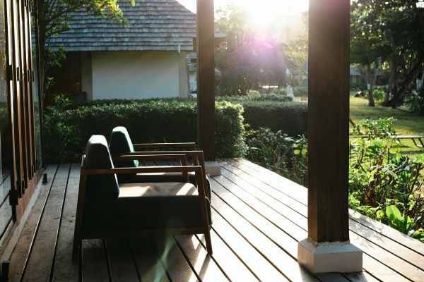 Peaceful wooden deck patio with chairs, lush greenery and sunlight.