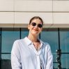 Young woman in sunglasses posing confidently in front of a modern glass building.