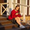 Young woman with a smartphone and coffee on wooden steps, enjoying the sunset.