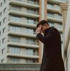 Elegant man in black coat standing in urban environment with modern buildings.