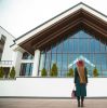 A woman with long hair stands fashionably outside a modern architectural building.
